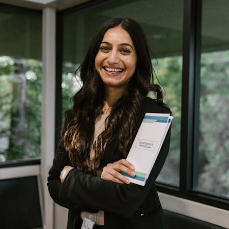 Confident woman holding conference program, smiling in modern indoor setting.