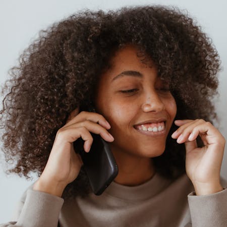 Smiling woman with afro hair enjoying a phone call indoors, wearing a casual sweater.