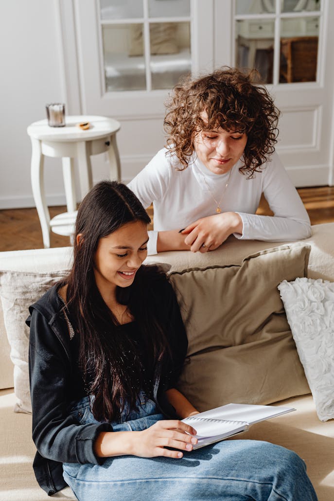 Two women enjoying a friendly and relaxed conversation indoors with a notebook.