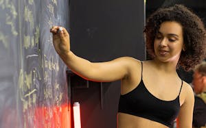 A woman with curly hair writes equations on a blackboard, focused and teaching.