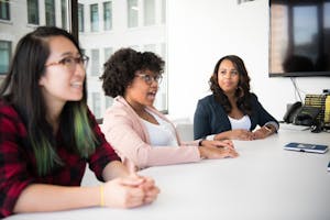 Three diverse women discussing in a bright office, highlighting teamwork and collaboration.