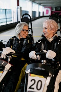 Two senior women having fun racing go-karts indoors, sharing smiles and friendship.